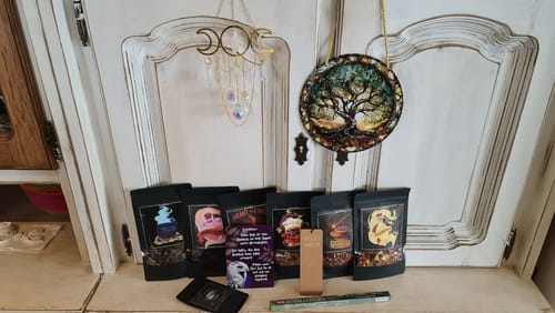 Rezensentin präsentiert HEM Räucherstäbchen und Teesorten vor einem rustikalen Schrank mit mystischer Dekoration.