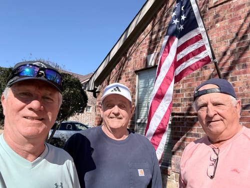 Three customers smiling outside in front of a brick wall with the Betsy Ross flag displayed.