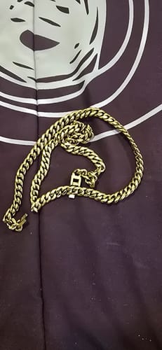 La Cadena Cuban Link Oro de un cliente, enrollada sobre una superficie oscura con un diseño gráfico.