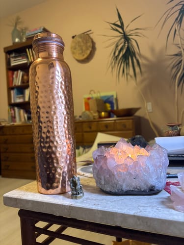Reviewer's hand-hammered Pure Copper Water Bottle on a table next to a glowing crystal candle holder.