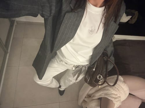 לקוחה מציגה את טי שירט LOUDER by Émily הלבנה כחלק מלבוש עם בלייזר אפור ומכנסיים לבנים.