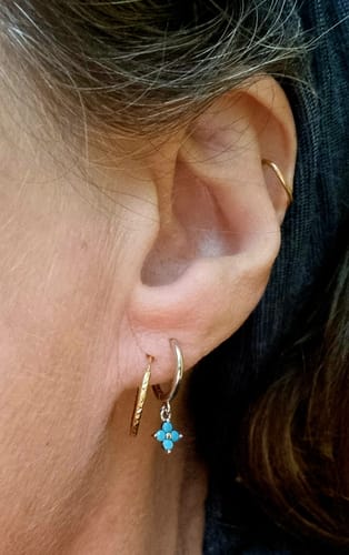 Close-up of a customer's ear wearing the Lucky Charm Aqua/Silver huggie with its turquoise four-leaf clover charm.