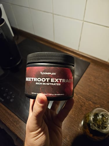 Customer holding a black jar of Complex Beetroot Extract in a kitchen.