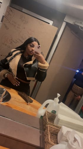 Reviewer in a mirror selfie wearing the black Sherpa Jacket, showing the vegan leather side with a cream sherpa collar.