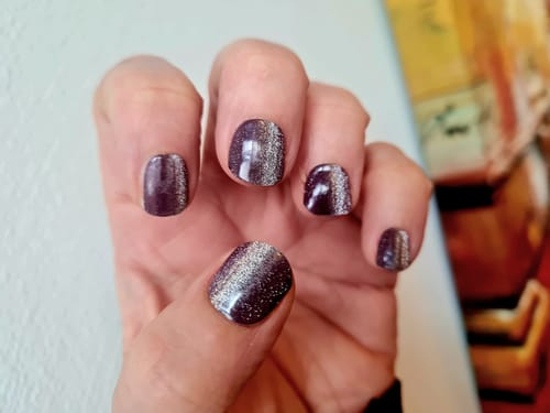 Hand einer Kundin, die die aufgetragenen 'Burgundy Cateye' UV-Gel-Nagelfolien mit starkem silbernem Effekt zeigt.