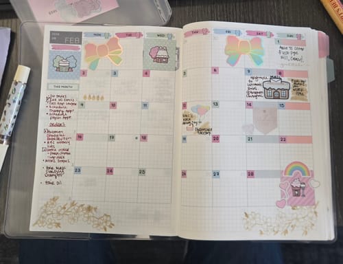 Reviewer's open planner showing a monthly view decorated with colorful stickers from the Hobonichi Subscription.