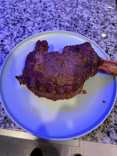 Customer's cooked bone-in cowboy ribeye from the Rancher Collection resting on a light blue plate.