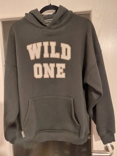 Rezensent zeigt den grünen Oversize-Hoodie „Wild One“, der an einem Kleiderbügel hängt.