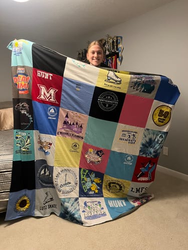A customer smiling while holding up her large, colorful Premium T Shirt Quilt made from skating t-shirts.