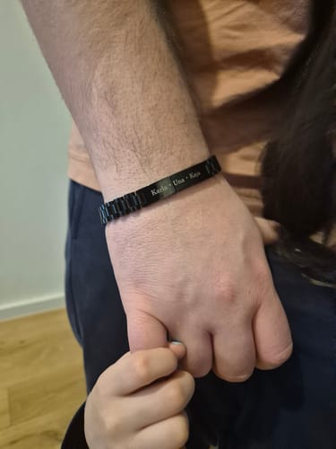 Customer wears the engraved black Imperium bracelet on their wrist while a child holds their hand.