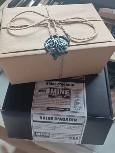 Recensore mostra la confezione del profumo BRISE D’AGADIR e una scatola regalo rustica legata con spago e ceralacca.