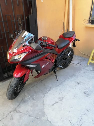 Un cliente muestra su motocicleta Kiwo Fuji 250 roja y deportiva estacionada en un patio.