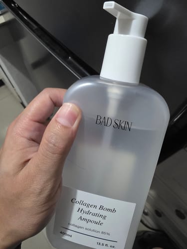 A customer's hand holding the large, translucent pump bottle of Bad Skin Collagen Bomb Hydrating Ampoule.