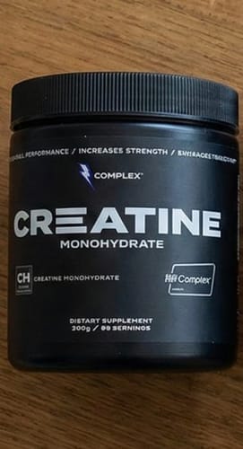 Customer's black tub of Complex Creatine Monohydrate supplement resting on a wooden surface.