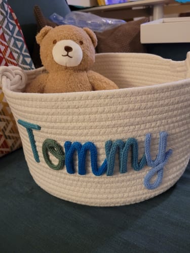 Customer's white woven basket, personalized with the name 'Tommy' in colorful yarn and holding a teddy bear.