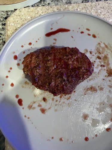 Reviewer's cooked Prime Top Sirloin steak resting on a white plate with juices.