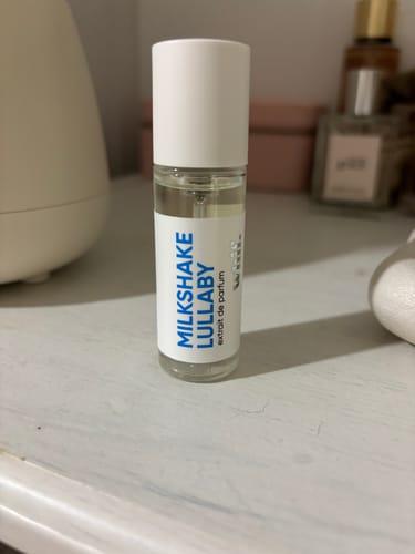 Customer's glass bottle of Milkshake Lullaby perfume with a white cap, standing on a white surface.