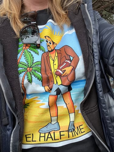 Reviewer wearing the El Halftime SB 60 OG T-Shirt, which has a colorful graphic of a character on a beach holding a football.