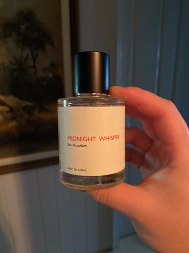 Customer holding a clear bottle of Midnight Whisper perfume with a black cap, showing it is half-used.