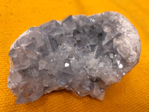 Photo d'un client : gros plan sur une géode de Célestine bleutée aux cristaux scintillants sur un tissu jaune.