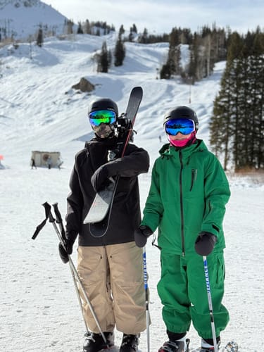 A customer wearing the tan Baggy Utility Snow Pants on a snowy ski slope with another person.
