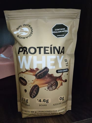 Cliente muestra la bolsa de su Proteína Whey -Café en un estante oscuro.