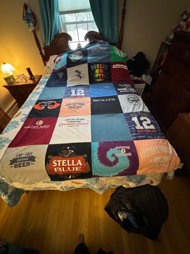 Customer's finished Premium T Shirt Quilt, made from many colorful t-shirts, spread across a bed.