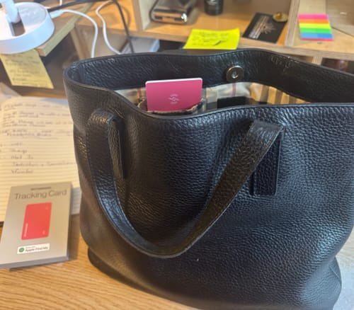 Customer's pink SPOTMINDERS Tracking Card peeking out of a black handbag, with the packaging on the desk.