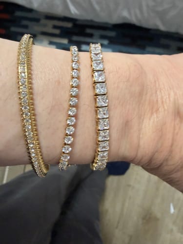 Close-up of a reviewer's wrist wearing the Luxe Tennis Bracelet stacked with two other gold bracelets.