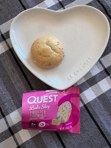 Un biscuit givré Quest d'un client sur une assiette en forme de cœur, à côté de l'emballage rose du biscuit.