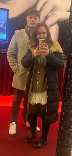 Kundin in einem Spiegelbild, die den Oversized-Cardigan „CozyGlam“ mit goldenen Knöpfen unter einer offenen schwarzen Jacke trägt.