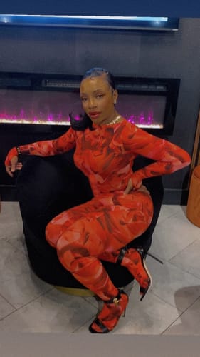 Customer sitting indoors wearing the red abstract print Bare Body Print Closed Toe Leggings.