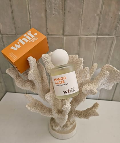 Reviewer's Mango Glaze perfume bottle and its orange box displayed artistically on a white decorative coral.