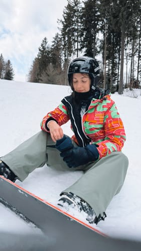 Customer wearing the baggy snow pants while sitting on a snowy slope with a snowboard.