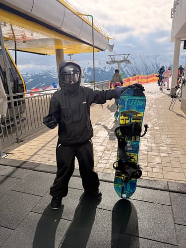Reviewer wearing the black baggy snow pants at a ski resort, standing with a snowboard.