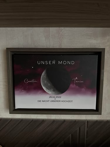 Rezensent zeigt die personalisierte Leinwand mit Mondmotiv, Namen und Hochzeitsdatum in einem dunklen Rahmen.