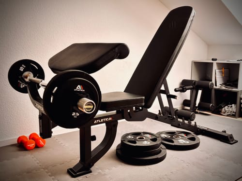 Kundenbild der schwarzen B2 Hantelbank mit ArmMaster-Anbau und einer Langhantel in einer Heimumgebung.