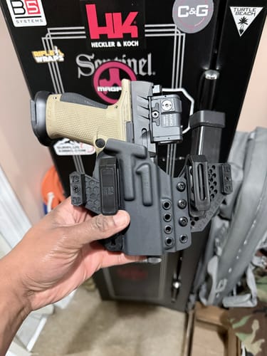 Customer holding the black APX holster, fitted with a tan pistol with a red dot sight and an extra magazine.