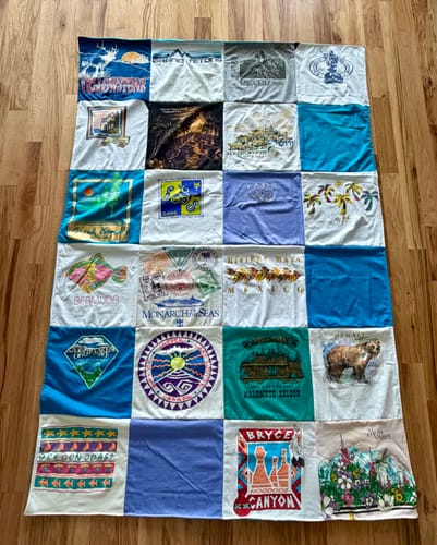 Customer's colorful Premium T Shirt Quilt made from travel t-shirts, laid out flat on a wood floor.