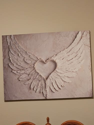 Customer's textured Angel Wings Wall Art with a heart-shaped design hung on a bedroom wall.