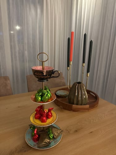 Klant toont de kleurrijke POLSPOTTEN Grandpa Etagère op een houten tafel, gevuld met paaschocolaatjes.