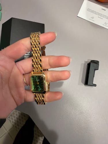 Customer holding the CLAIRE DE MAINS watch, showing its gold woven band and rectangular green face.