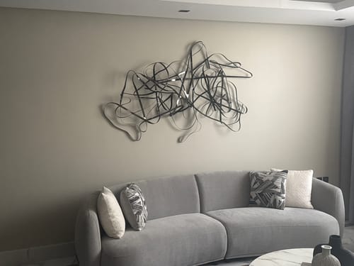 Customer's modern Hand Crafted Stainless Steel Artwork mounted on a living room wall above a grey sofa.