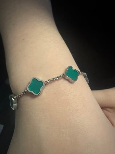Customer wearing a silver-colored bracelet with green, clover-shaped charms on their wrist.