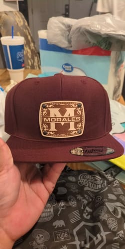 Customer holding a maroon Monogram Custom Hat with a leather patch engraved with 'M' and 'MORALES'.
