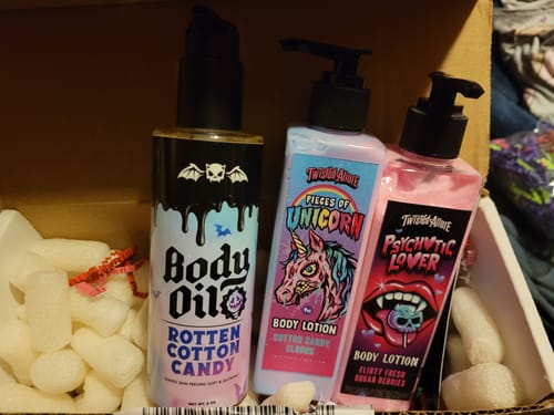 Reviewer's bottle of Rotten Cotton Candy Body Oil next to two scented body lotions in a shipping box.
