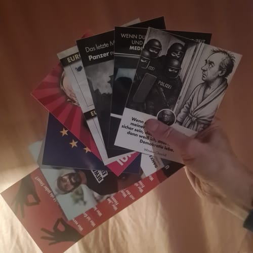 Ein Rezensent hält die bestellten satirischen Aufkleber fächerartig in der Hand.