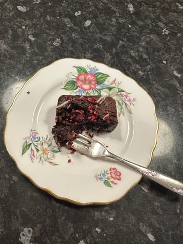 Customer's half-eaten raspberry brownie from their mixed box, served on a decorative floral plate with a fork.
