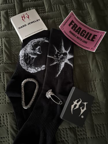 Customer's Hard Jewelry packaging, socks, and silver-colored jewelry pieces displayed on a green quilted surface.
