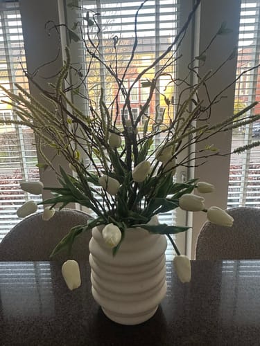 Klant toont het boeket warm witte tulpen, gearrangeerd met decoratieve takken in een witte vaas.